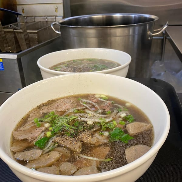 Two bowls of Vietnamese pho with beef, noodles, and herbs in a restaurant kitchen setting.