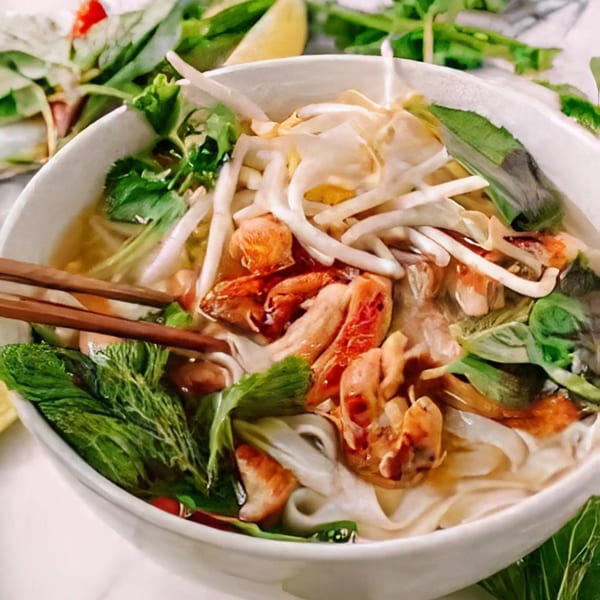 A close-up of a bowl of Vietnamese pho with noodles, shrimp, bean sprouts, and fresh herbs.