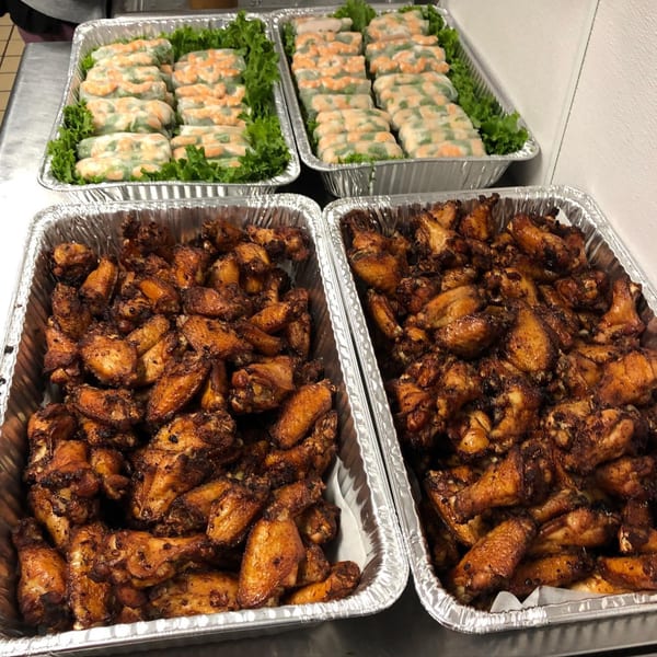 Two foil trays of shrimp spring rolls and two foil trays of chicken wings.