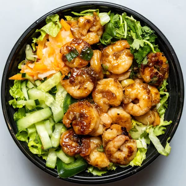 Top-down view of a YUMMI BANH MI STREETSIDE CAFÈ shrimp bowl with lettuce, cucumbers, and carrots.