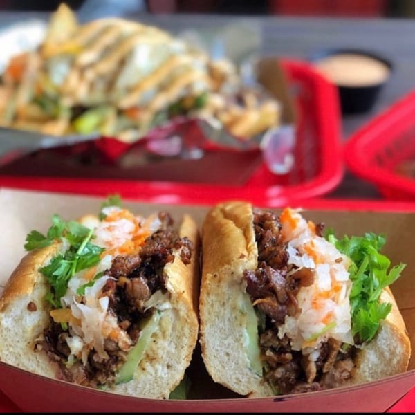 Two halves of a Vietnamese banh mi sandwich with meat, pickled vegetables, and cilantro.