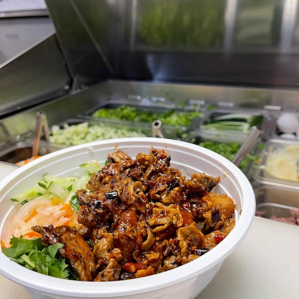 A Vietnamese bowl with glazed meat, pickled vegetables, and fresh herbs, ready to be served.