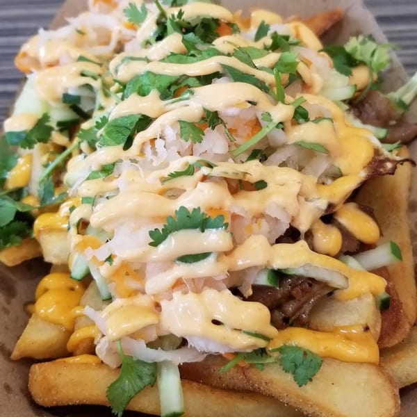 Vietnamese-style loaded fries with meat, pickled vegetables, cilantro, and a creamy orange sauce.