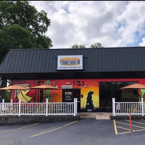 The exterior of Yummi Banh Mi, a Vietnamese cafe with a vibrant mural and outdoor seating.