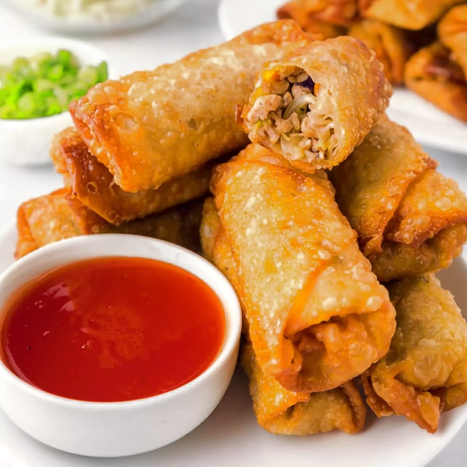 Crispy Vietnamese egg rolls with savory filling, served with a side of sweet chili dipping sauce.