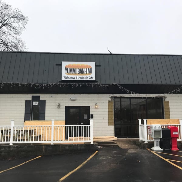 Exterior of Yummi Banh Mi Vietnamese Streetside Café with a white sign and dark roof.